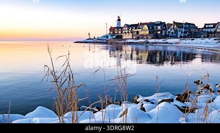 Ruhiger Wintersonnenuntergang über dem Küstendorf mit Leuchtturm und ruhigen Gewässern, Urk Niederlande Stockfoto