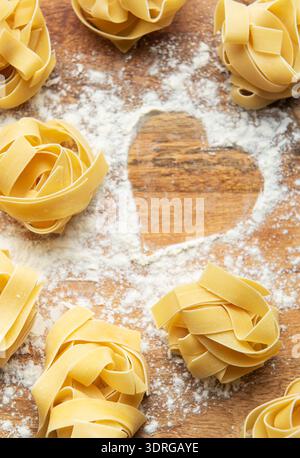 Ungekochte Tagliatelle-Pasta nestet mit Mehlherz auf Holzbrett Stockfoto