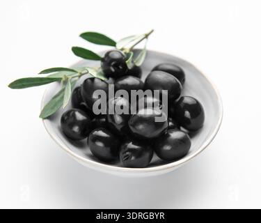 Schwarze Oliven mit Blättern in einer Schüssel auf weißem Hintergrund Stockfoto
