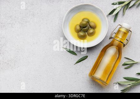 Olivenölflasche und Schüssel mit grünen Oliven und Olivenzweigen auf Marmorhintergrund Stockfoto