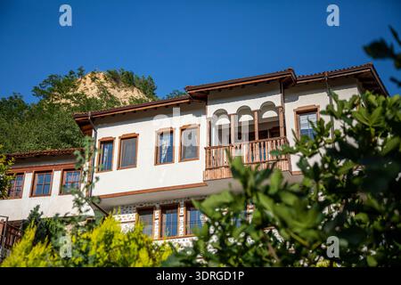 Ein traditionelles bulgarisches weißes Haus in Melnik-Stadt mit einem Holzbalkon und gerahmten Fenstern befindet sich auf einem sonnendurchfluteten Hügel, umgeben von üppigem Grün, Sho Stockfoto