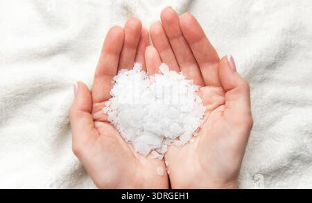 Frau, die weiße Magnesiumchloridflocken in den Händen hält, um ein entspannendes Bad zu nehmen Stockfoto