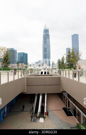 Modernes urbanes plaza mit Rolltreppen, die zu einem erhöhten Fußweg führen, hoch aufragende Wolkenkratzer im Hintergrund unter bewölktem Himmel Stockfoto