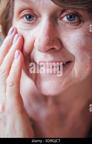 Nahaufnahme des Gesichts einer Reifen Frau, die eine feuchtigkeitsspendende weiße Creme aufträgt. Eine ältere Dame kümmert sich um ihre Gesichtshaut. Ein Stift Stockfoto