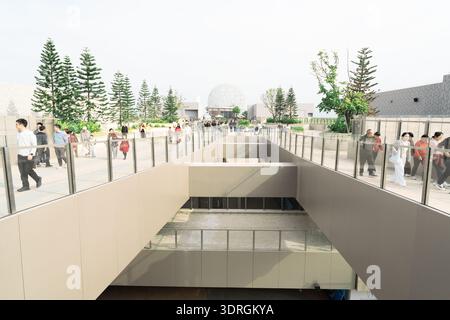 Moderne Fußgängerbrücke mit Glasgeländern und Spaziergängen, mit Bäumen und Kuppelstruktur im Hintergrund unter klarem Himmel Stockfoto