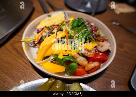 Vietnamesischer Sommerbrötchen-Salat mit Garnelen, Mango, Tomaten und frischem Gemüse auf Holztisch Stockfoto