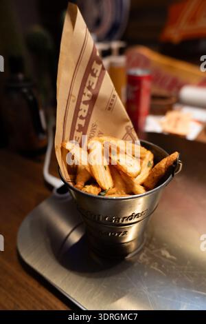 Knusprige Pommes Frites in Metallkübel mit Papierkegel, serviert auf Holztisch im Restaurant Stockfoto