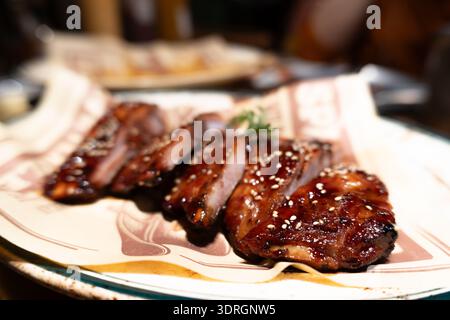 Koreanische Grillgerippchen mit Sesam auf gemustertem Teller, Restaurant-Ambiente Stockfoto