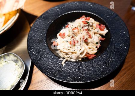 Italienische Pasta mit Tomaten und Käse in schwarzer Keramikschale auf Holztisch Stockfoto