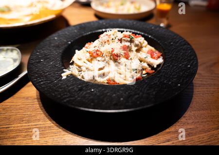 Italienische Pasta mit cremiger Sauce und Tomatengarnitur, serviert in Black Bowl auf Holztisch Stockfoto