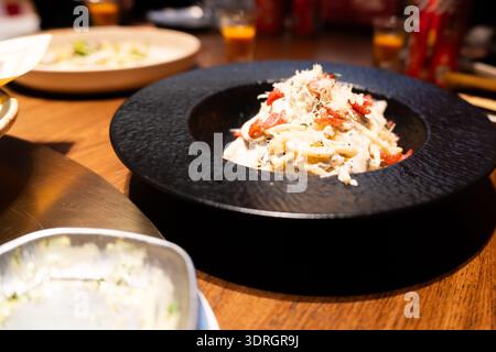 Italienische Pasta mit Krabbenbelag in schwarzer Keramikschale auf Holztisch Stockfoto