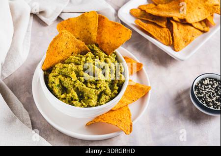 Köstliche Guacamole in einer Schüssel und Tortilla Chips auf einem Teller auf dem Tisch Stockfoto