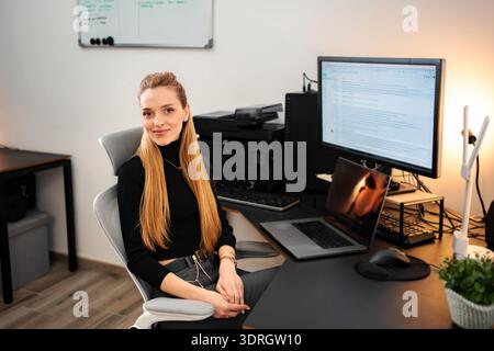 Junge Frau lächelt im modernen Home-Office-Arbeitsplatz Stockfoto