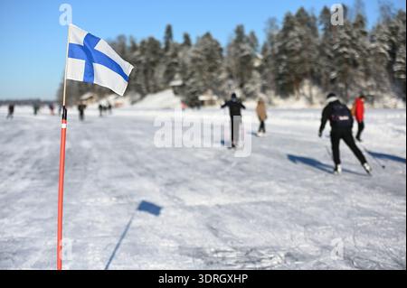 Tuusulasee, Finnland – 14. Februar 2026: Eine Winterszene, die eine finnische Flagge zeigt, die eine Eislaufstrecke auf der gefrorenen Oberfläche des Sees markiert Stockfoto