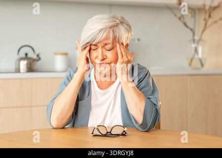 Kopfschmerzen, unglückliche Seniorin mittleren Alters, die an Kopfschmerzen leidet, krank, die Schläfen zu Hause reibt. Reifer alter Seniorengroßmot Stockfoto