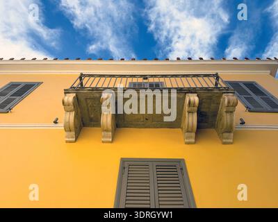 Gelbe neoklassizistische Gebäudefassade mit flachem Blick, Holzladenfenster und Marmorbalkon, blauer bewölkter Himmel. Plaka, Athen, Griechenland Stockfoto