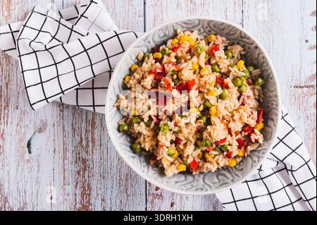 Nahaufnahme von hausgemachtem gebratenem Reis mit Erbsen, Mais und Pfeffer in einer Schüssel auf dem Tisch Stockfoto