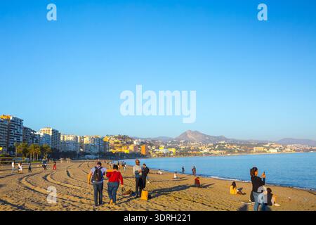 Malaga, Spanien – 10. Februar 2020: Familien und Touristen genießen die Sonne am Strand von La Malagueta mit hohen Wohnhäusern und einem Volleyballnetz Stockfoto