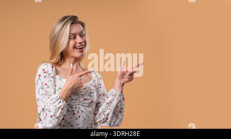 Glückliche Lächelnde Frau, Die Etwas Isoliertes Auf Beige Zeigt Stockfoto
