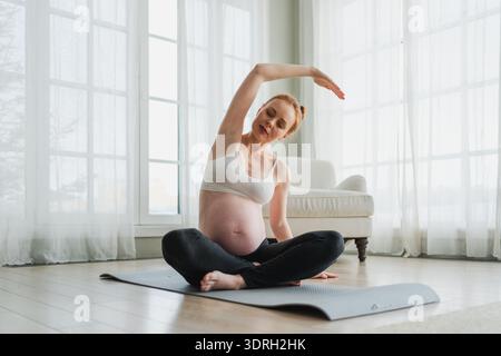 Schwangerschafts-Yoga-Fitnesstraining. Schwangere Frau, die zu Hause Yoga praktiziert. Schwangere Frau, die Sport auf Yogamatte macht Stockfoto