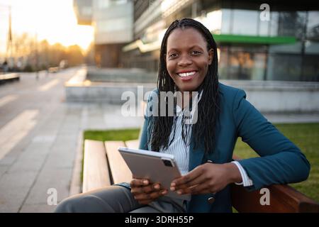 Afroamerikanische Geschäftsfrau, die draußen am Tablet arbeitet und lächelt Stockfoto