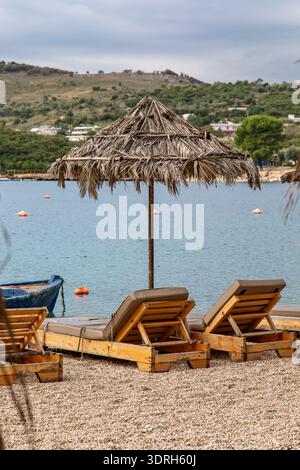 Leere Liegen unter Strohschirm nach der Tourismussaison im Ferienort Ksamil, Albanien Stockfoto