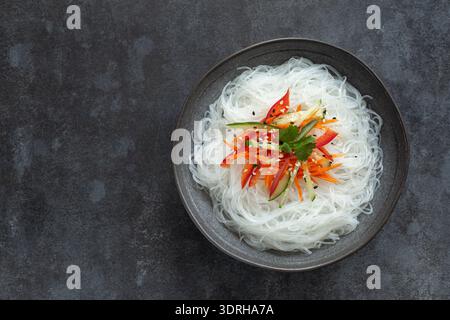 Funchoza-Glas-Reisnudeln mit Gemüse in dunkler Schüssel, dunkler Hintergrund, Draufsicht, Kopierraum Stockfoto