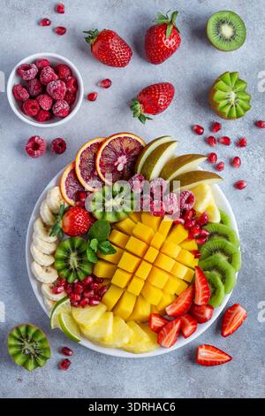 Obst- und Beerenplatte, Mango, Ananas, Birne, Kiwi, Orange, Banane, Erdbeere, Himbeere auf weißem Teller, Draufsicht Stockfoto