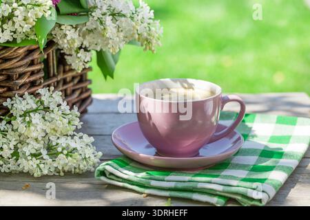 Kaffeetasse und bunte Fliederblüten auf dem Tisch Stockfoto