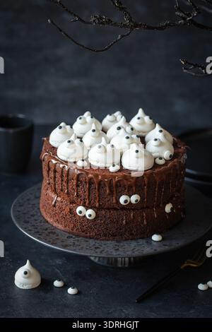 Gruseliger Halloween-Schokoladenkuchen mit Meringue-Geistern und Bonbonaugen. Dunkler Hintergrund Stockfoto