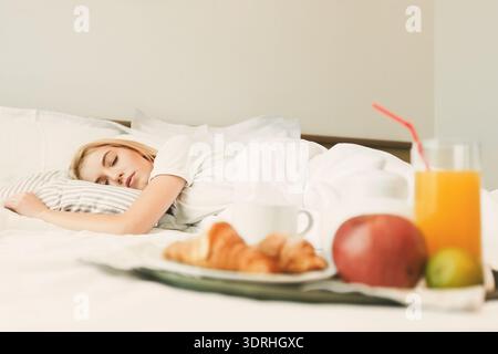 Frau, die sich in einem Bett mit Frühstück auf der Seite in einem gemütlichen Zimmer ausruht Stockfoto