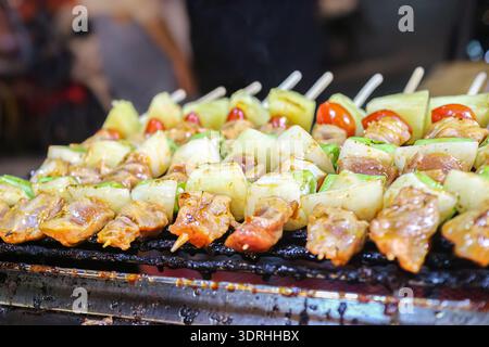 Nahaufnahme von Hühnchen- und Gemüsespießen auf einem Holzkohlegrill. Authentische thailändische Street-Food-Bilder für kommerzielle Menüs, Food-Blogs und Reisemarketing. Stockfoto