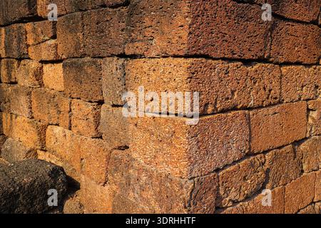 Detail einer alten lateritalen Wandecke. Rötlich-braune poröse Steinstruktur, die historische asiatische Architektur und strukturelle Stabilität repräsentiert. Stockfoto