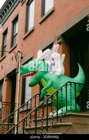 Ein aufblasbarer Dinosaurier steht auf den Stufen eines Ziegelgebäudes mit einer Hasenfigur auf dem Rücken während der Tageslichtstunden. Stockfoto