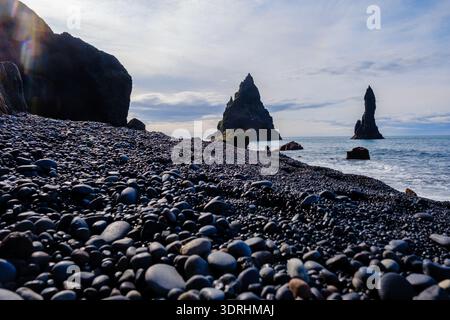 Am Reynisfjara Beach in Island bedecken glatte schwarze Kieselsteine das Ufer, während sich gewaltige Meeresberge dramatisch aus dem oc erheben Stockfoto