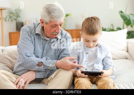 Glückliche Familie zu Hause. Alter Seniorenmann Großvater Junge Enkel genießt gemeinsame Zeit und sieht Video am Telefon. Gute Zeit zu Hause. Stockfoto