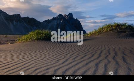 Majestätische Berglandschaft mit grasbewachsenen schwarzen Sanddünen in Island während der Dämmerung Stockfoto