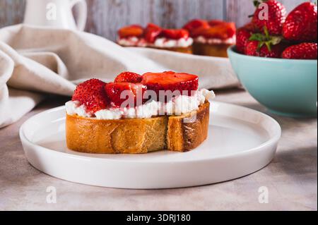 Gegrillter Toast mit Frischkäse und gedünsteten Erdbeeren auf einem Teller auf dem Tisch Stockfoto