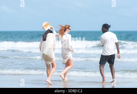 Gruppe von verschiedenen Freunden, die Spaß am Strand haben, laufen und an einem sonnigen Tag in den Wellen planschen Stockfoto
