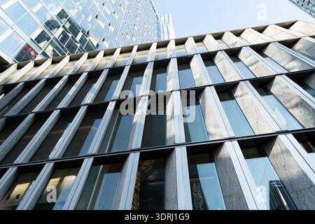 Moderner Glashochhaus mit reflektierenden Fenstern im urbanen Stadtbild, flacher Blick unter klarem Himmel Stockfoto