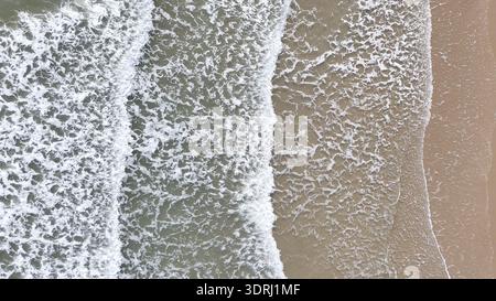 Aus der Vogelperspektive auf sanfte Meereswellen, die sich auf einen Sandstrand stürzen Stockfoto