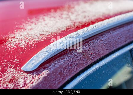 Außendetail des Winterwagens mit Eispartikeln auf dem glänzend roten Dach um silberne Dachreling und Fensterkante, abstrakter Hintergrund mit Fahrzeugstruktur Stockfoto