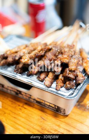 Chinesische Grillspieße auf Metalltablett am Street Food Stand mit Holztischhintergrund Stockfoto