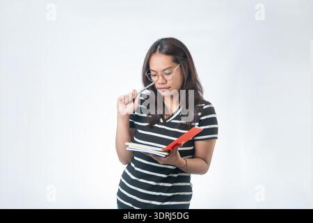 Konzentrierter indonesischer Student in Brille, der den Stift an der Stirn hält, während er Notizen liest. Konzept für harte Arbeit, Prüfungsvorbereitung und gezieltes Lernen. Stockfoto
