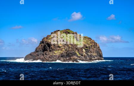 Die Insel Roque de Garachico entspringt dem Atlantik bei Garachico, Teneriffa, den Kanarischen Inseln, Spanien. Die vulkanische Gesteinsformation steht isoliert im blauen Wasser vor einem sonnigen Himmel. Stockfoto
