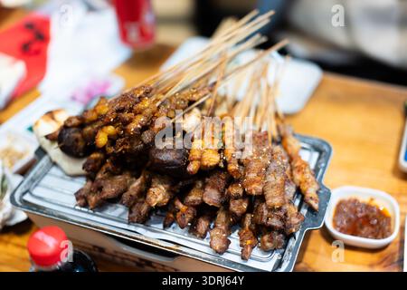 Indonesische Satay-Spieße auf Metalltablett mit Erdnusssauce, serviert auf Holztisch im Restaurant Stockfoto