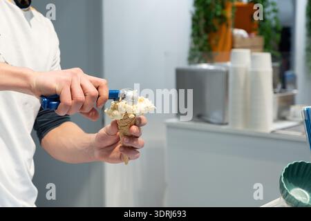Eisverkäufer, der cremiges Dessert in einem lebhaften Dessertladen in Waffelkegel einpackt Stockfoto
