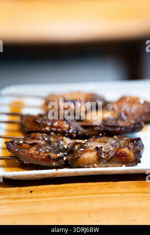 Gegrillte japanische Yakitori-Spieße mit Sesam auf weißem Teller, serviert auf Holztisch Stockfoto