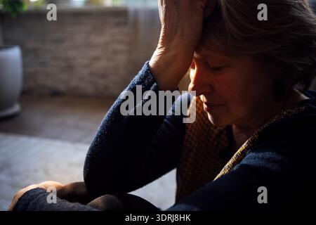 Nahaufnahme einer älteren Frau mit Kopfschmerzen. Eine reife Dame sitzt auf dem Boden Stockfoto