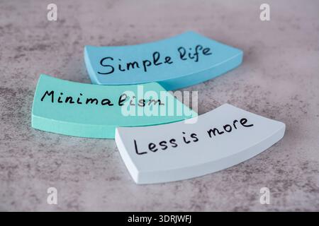 Minimalismus, weniger ist mehr, einfache Lebenswörter mit schwarzen Buchstaben auf den bunten Holzbrettern auf grauem Hintergrund geschrieben. Stockfoto